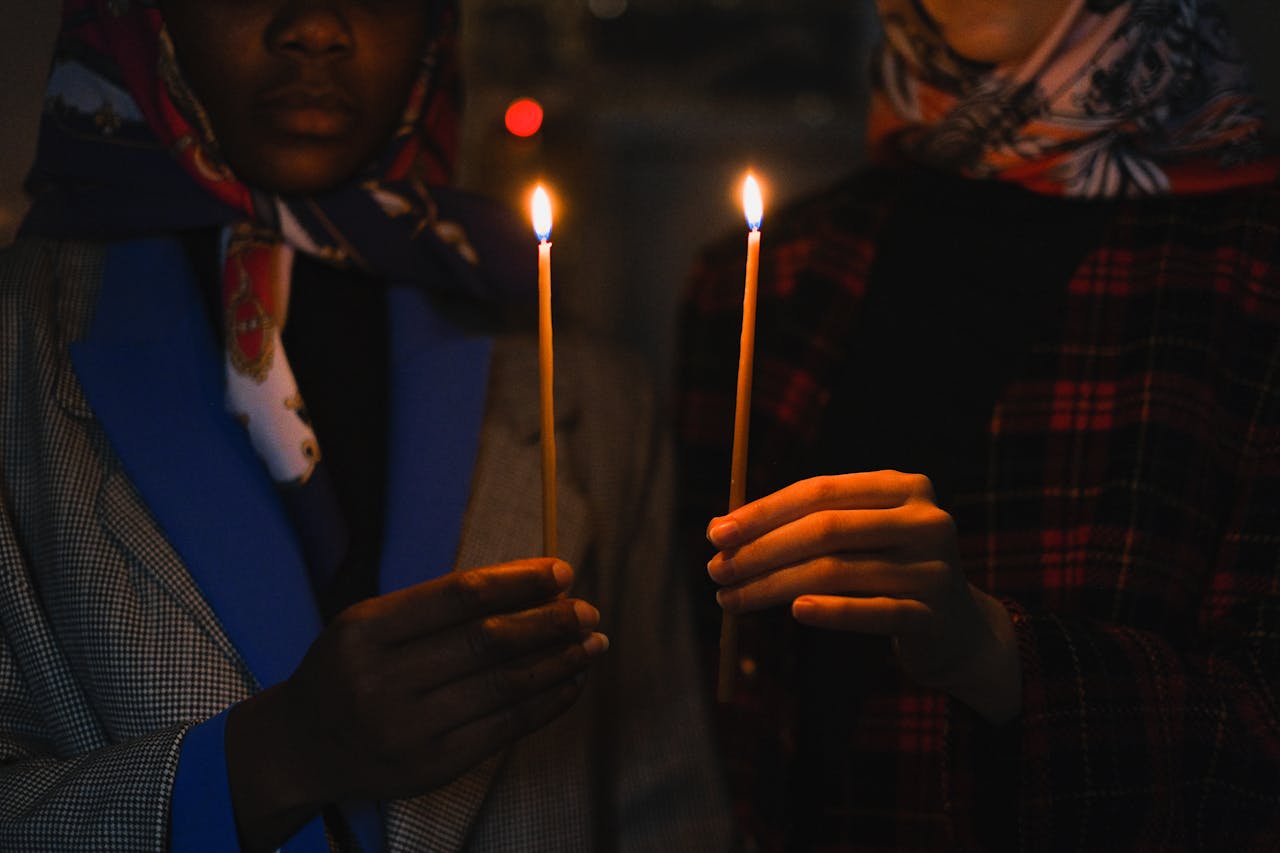 Two individuals holding candles in dark, religious ambiance.